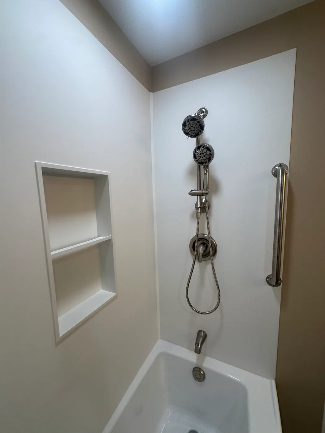 White tub and shower surround with a stainless grab bar, multi-function shower head and a recessed double niche