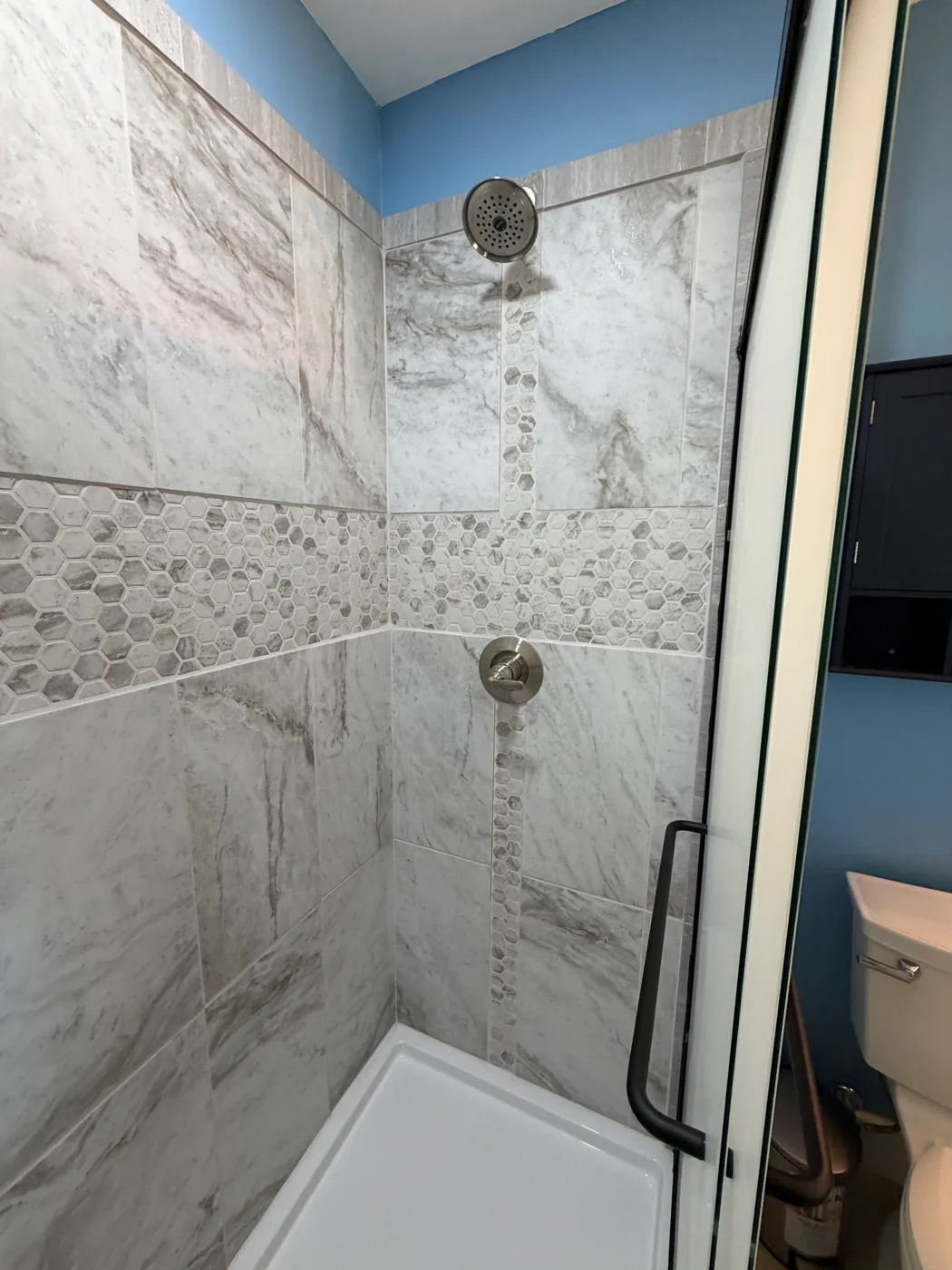 Marble-look tile shower with a hexagon mosaic accent strip and brushed nickel fixtures