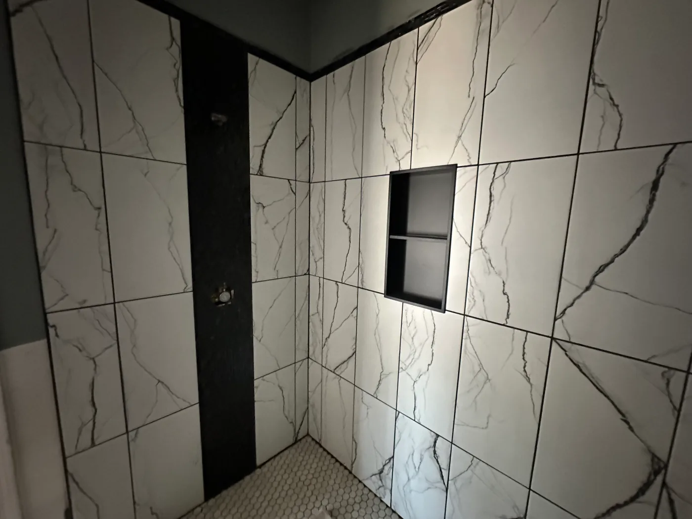 Marble-look tile shower with a recessed niche and a dark vertical accent strip