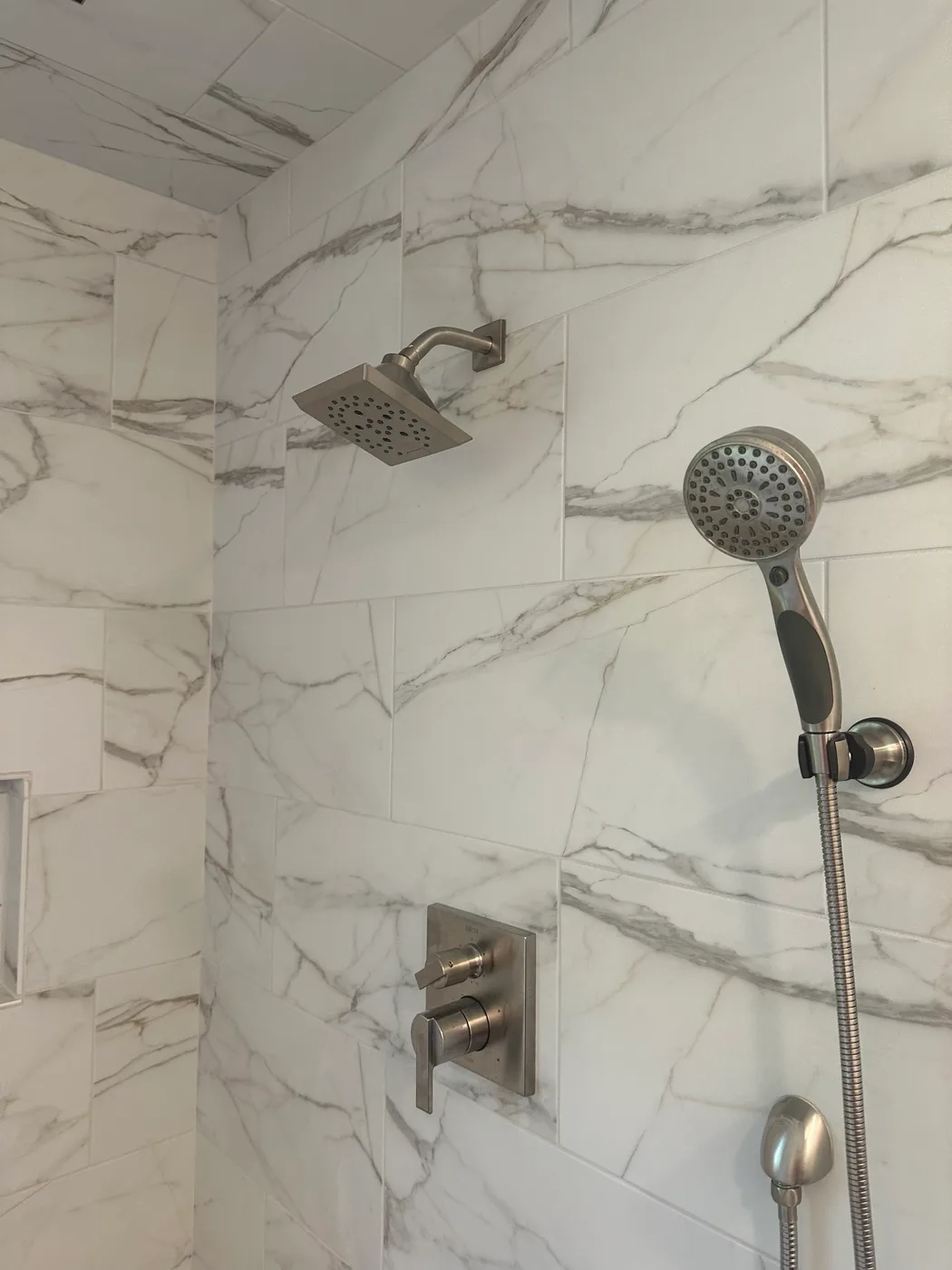 Marble tile shower with a square rain head, handheld sprayer and brushed nickel controls