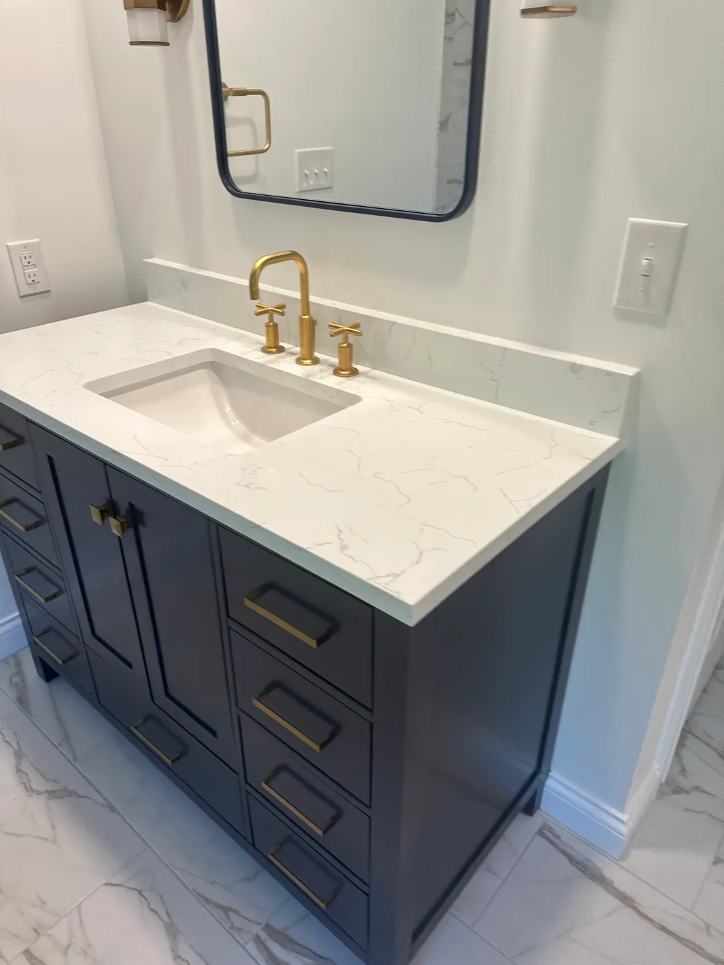 Navy double-drawer vanity with white marble countertop, gold cross-handle faucet and a framed mirror