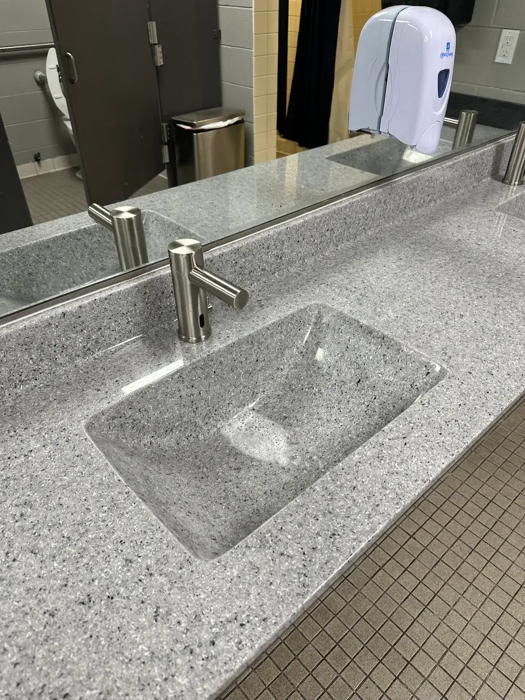 Molded terrazzo basin with a brushed nickel faucet in a commercial bathroom