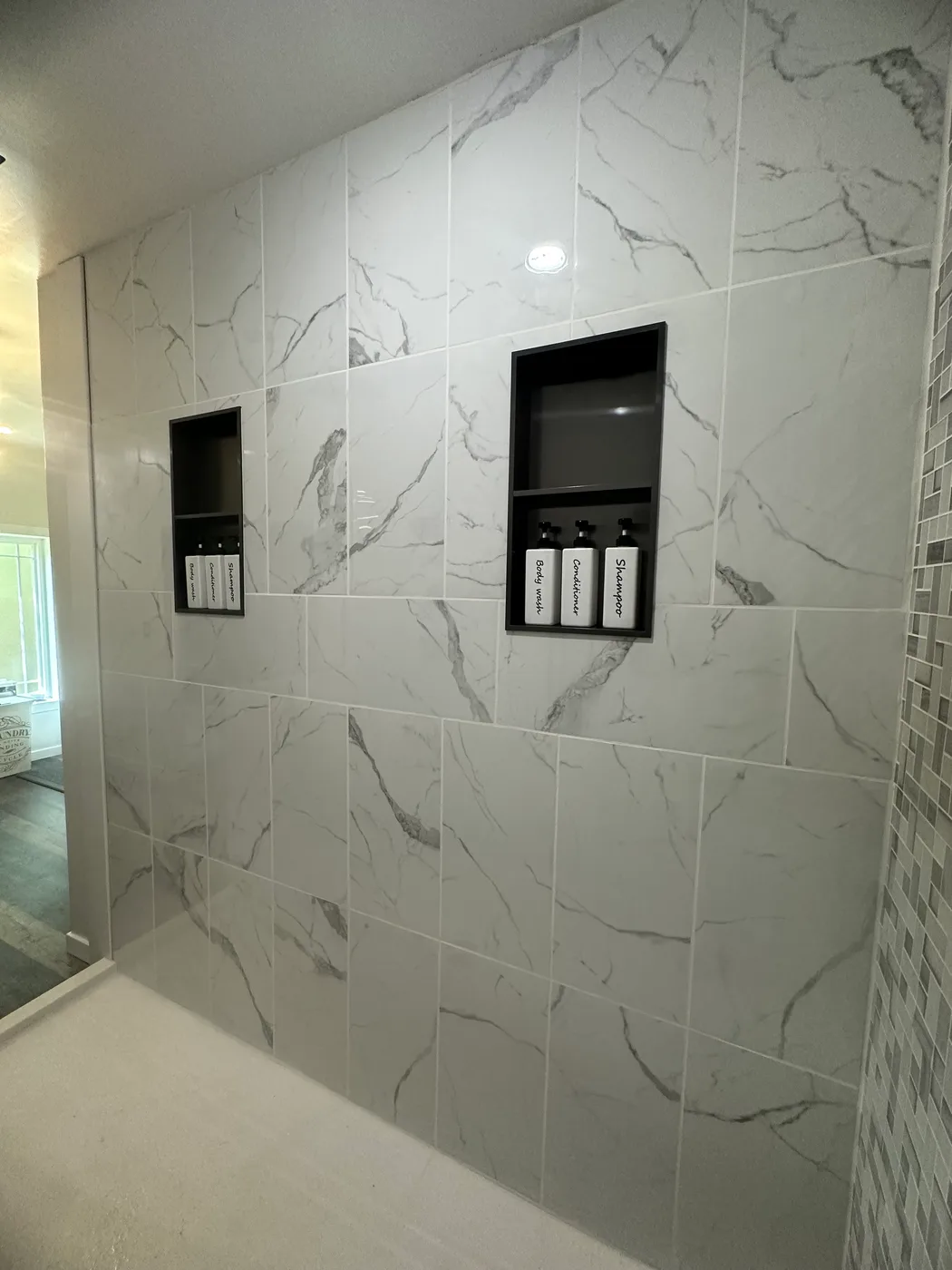 White marble tile shower with two recessed niches and a glass mosaic accent border