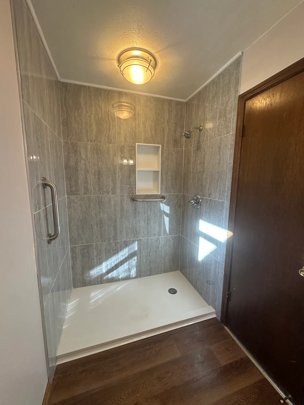 Finished walk-in tile shower with a recessed niche, grab bar and dual shower heads