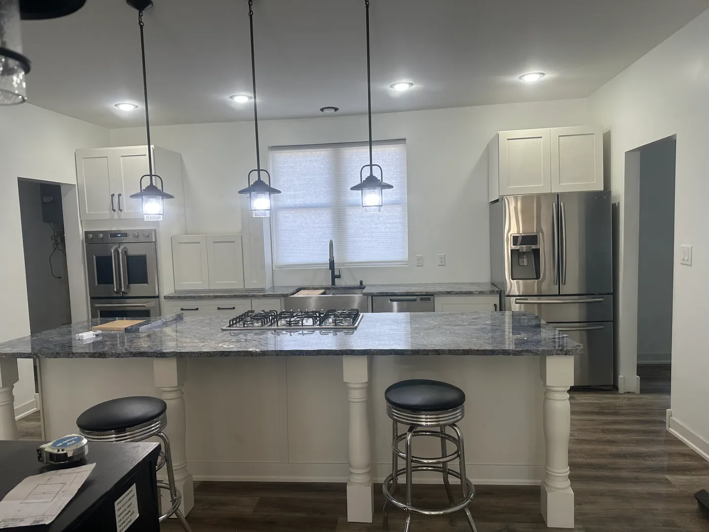 Finished kitchen with a gray granite island, lantern pendant lights, gas cooktop and stainless steel appliances
