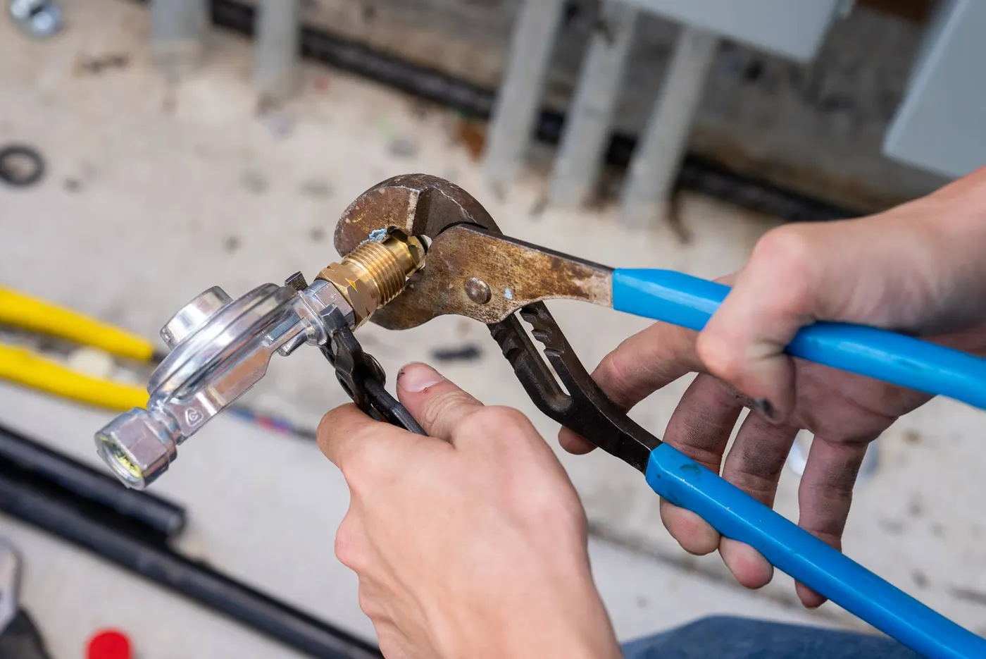 Hands tightening a gas fitting with channel-lock pliers