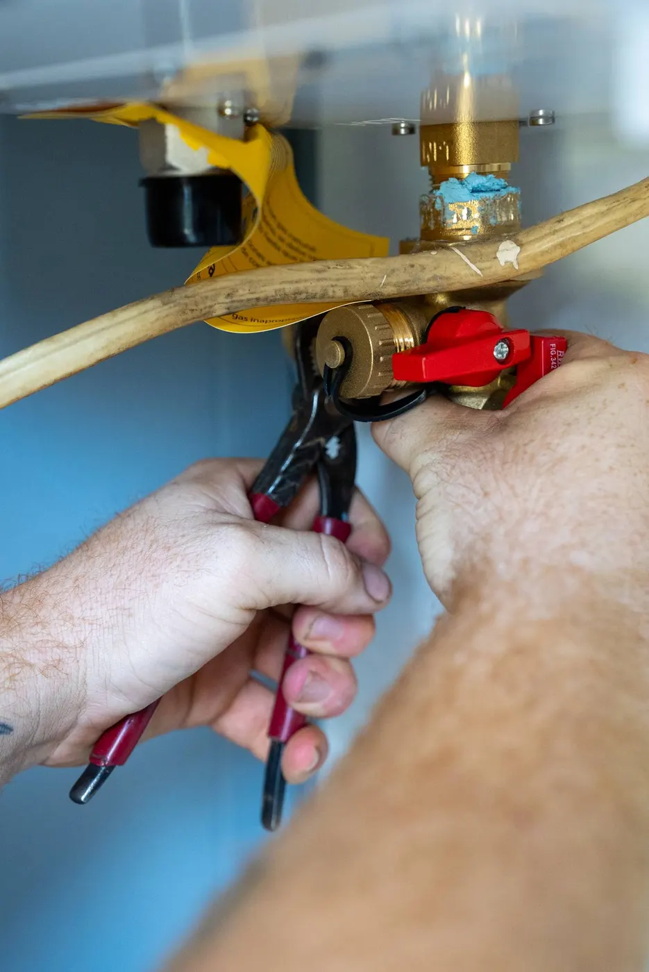 Hands using pliers on a tankless water heater valve