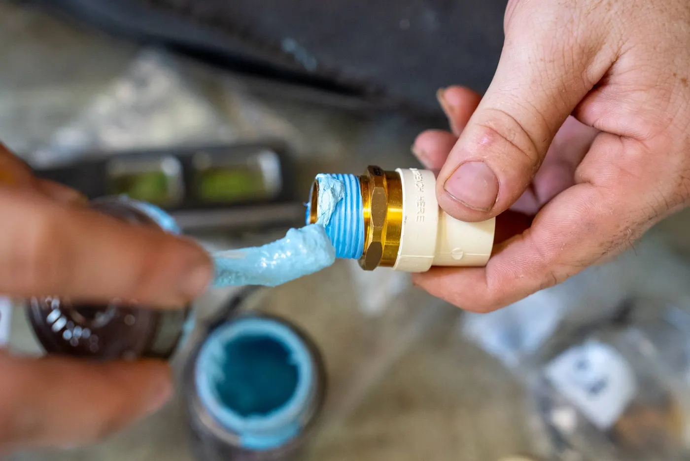 Hands applying thread sealant to a brass pipe fitting