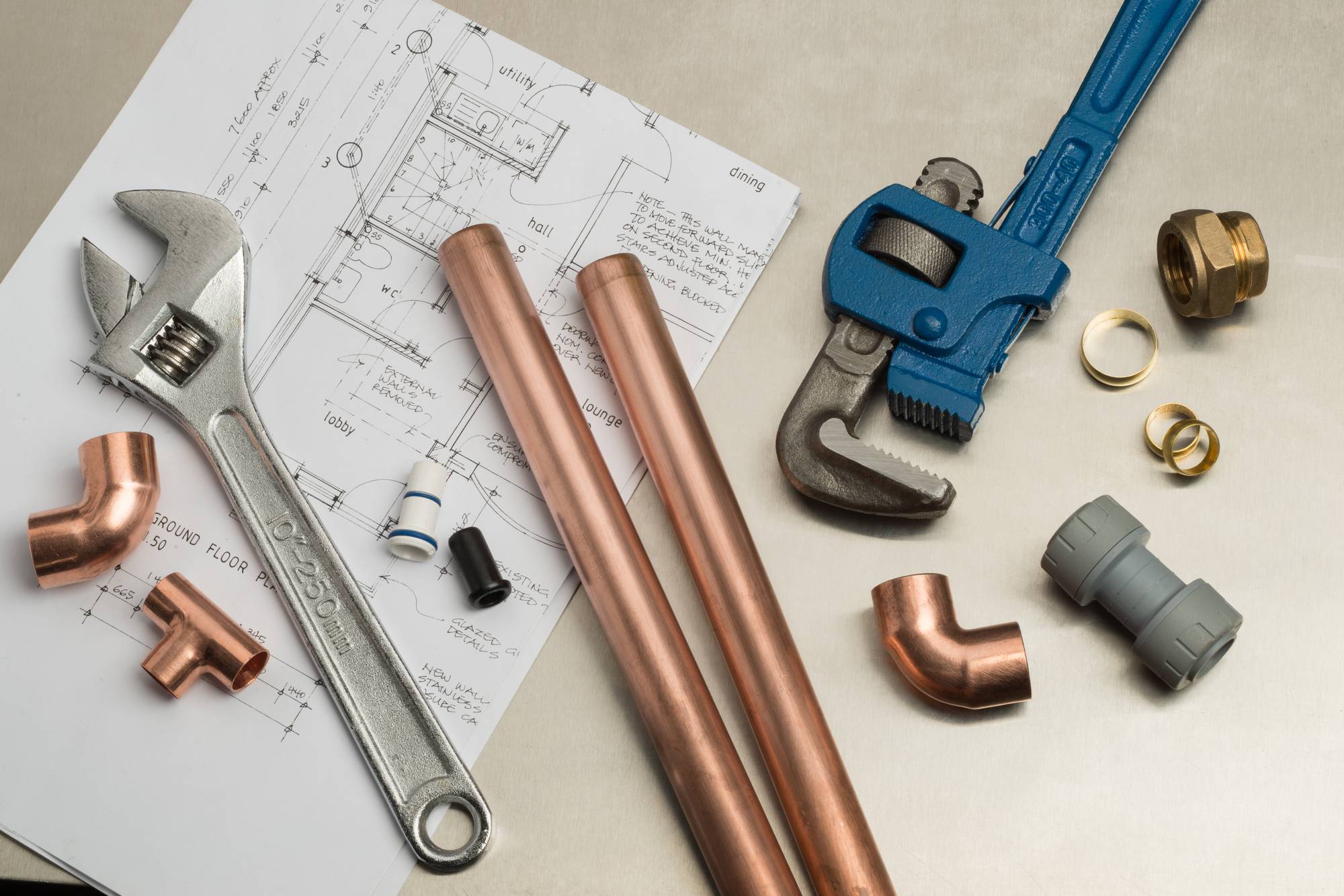 Pipe wrenches, copper pipe and fittings laid out over a set of house plans